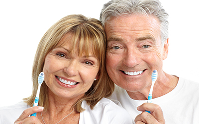an older man and woman smiling with toothbrushes
