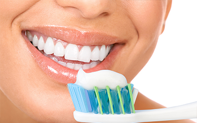 A woman smiling with a toothbrush and toothpaste in front of her smile