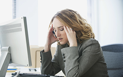 A woman sitting at the computer with her hands on her head looking stressed