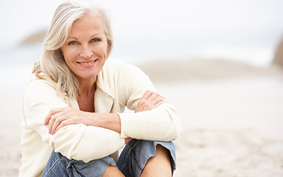 An older woman sitting on a beach smiling
